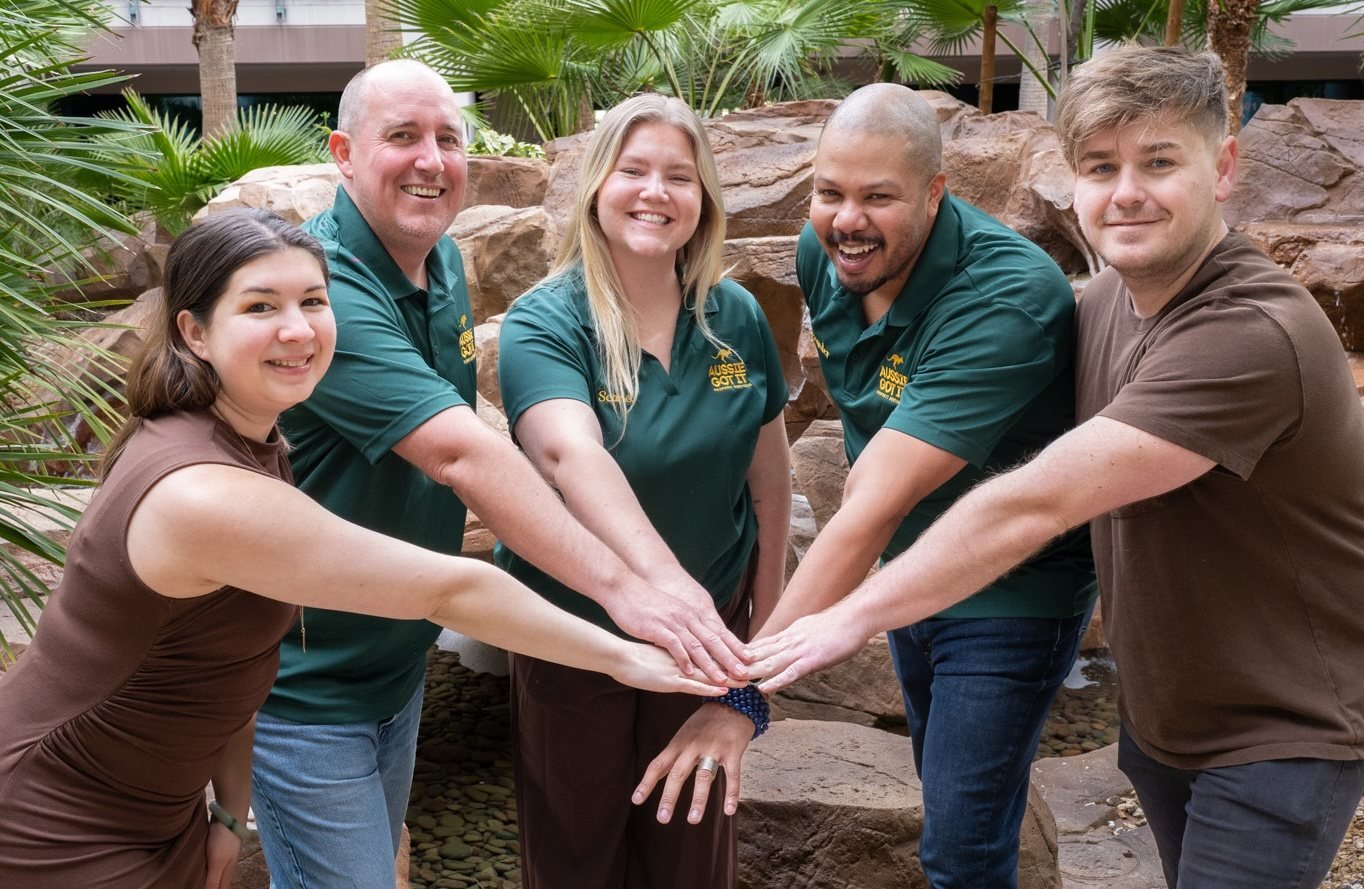 The AUSSIE GOT IT team in green and brown uniforms, hands stacked together in a courtyard